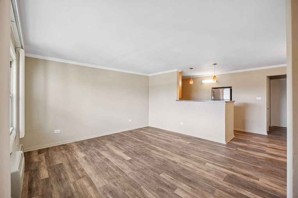 an empty living room with wood flooring and a kitchen