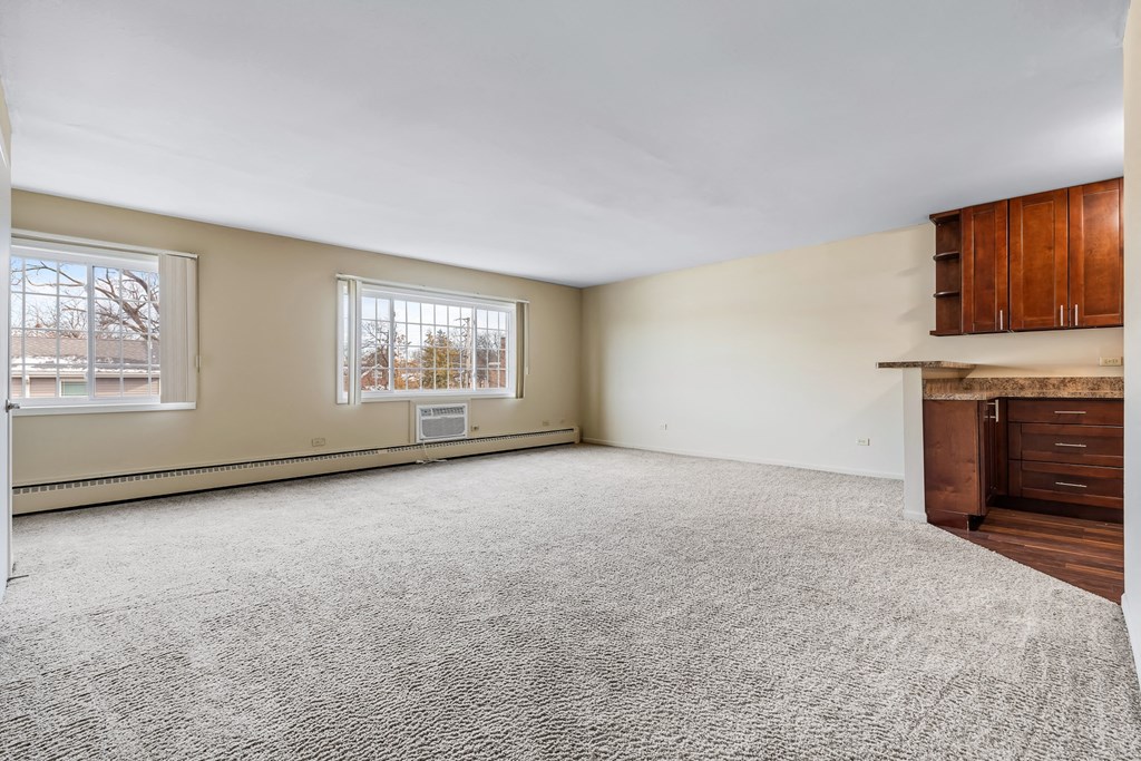 A large, empty room with a grey carpet and wooden furniture.