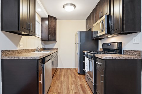 a kitchen with black appliances and wood flooring and black cabinets