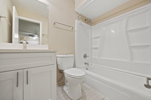 A white toilet sits in a bathroom next to a white bathtub.