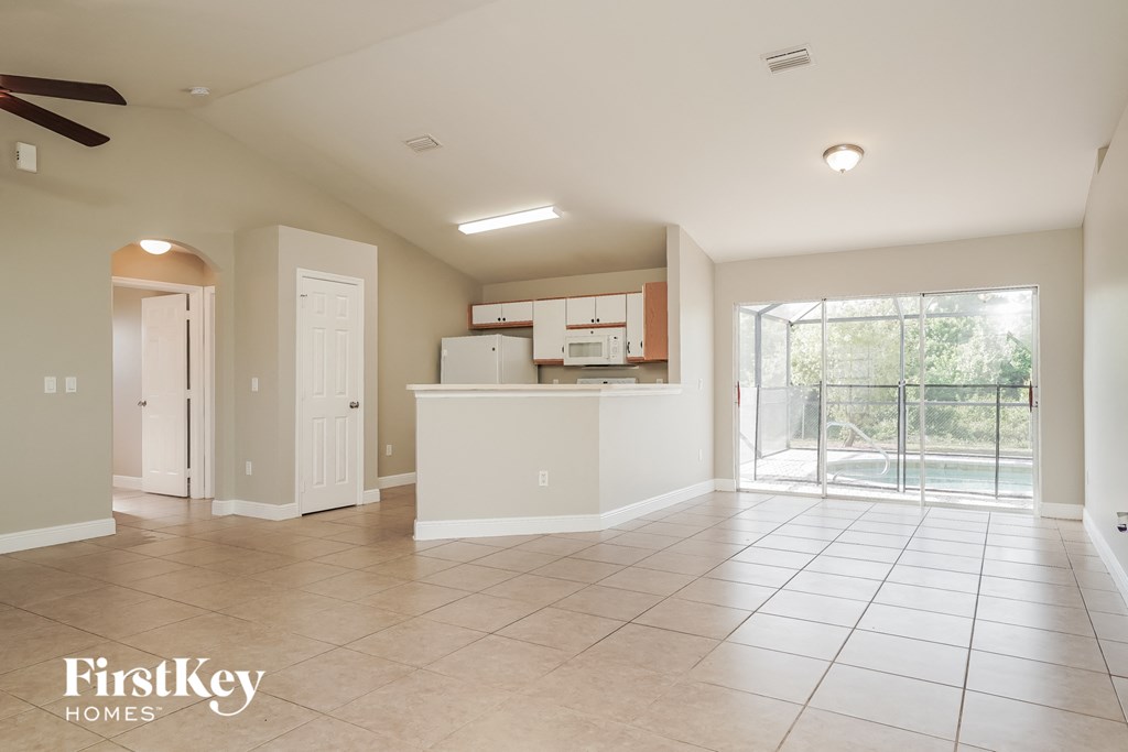 A spacious, empty room with a kitchenette and sliding glass doors leading to a balcony.