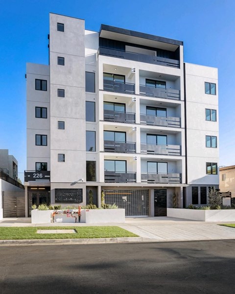 A modern multi-story building with balconies and a black gate in front.