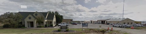 A building with a sign in front of it and cars parked in the background.