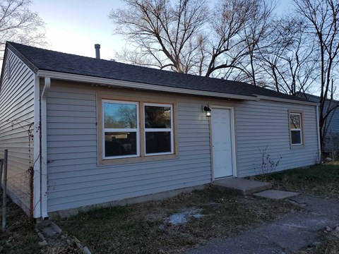 A small house with a grey siding and a white door is shown.