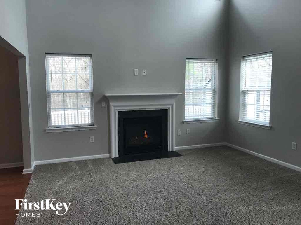 an empty living room with a fireplace and three windows