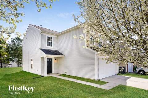 A white house with a black door and a tree with white flowers in front.