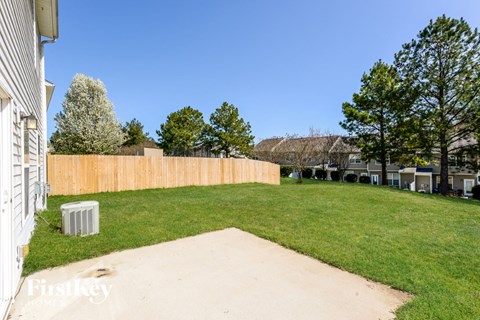 A backyard with a concrete pathway leading to a grassy area with a fence and trees.
