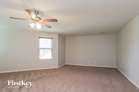 the spacious living room with ceiling fan and carpeting