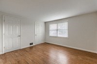 an empty bedroom with white walls and a window and wooden floors
