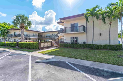 an empty parking lot in front of an apartment building with palm trees