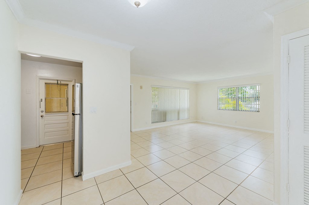 an empty living room with a door to the kitchen and a tiled floor