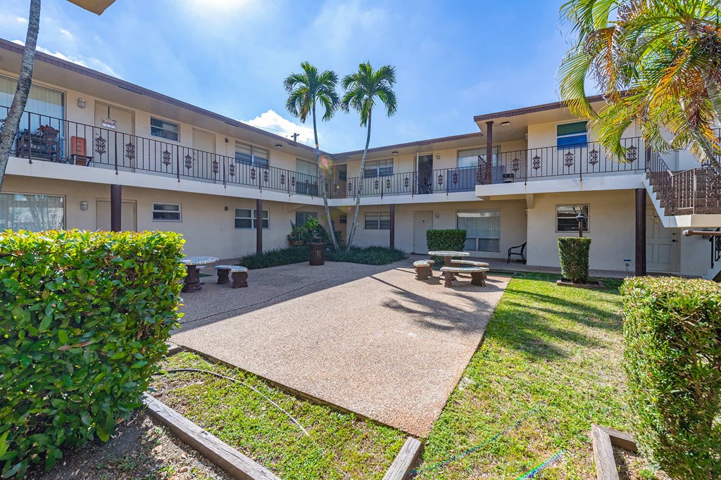 a courtyard with benches and palm trees in front of a building