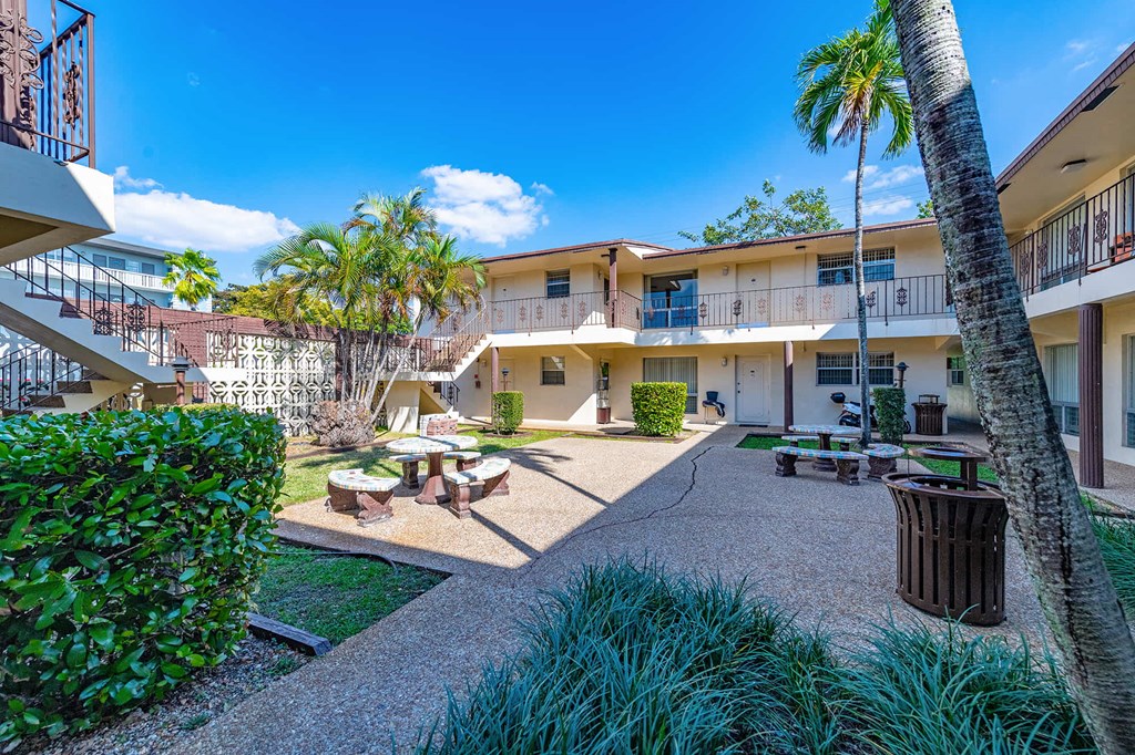 a courtyard with tables and benches and palm trees