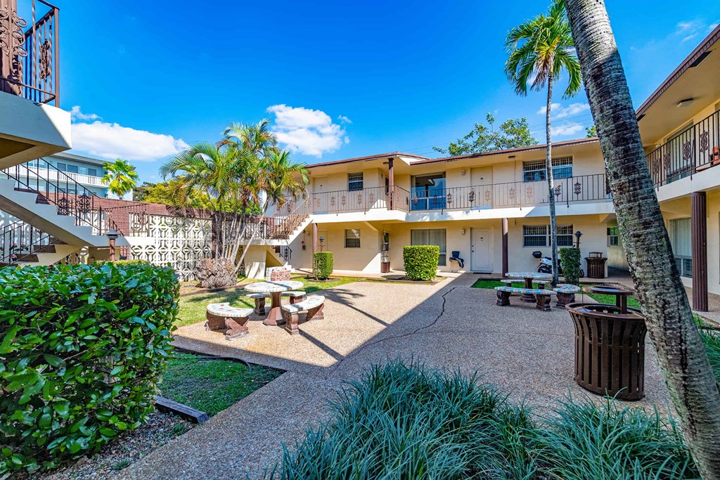 a courtyard with tables and benches and palm trees