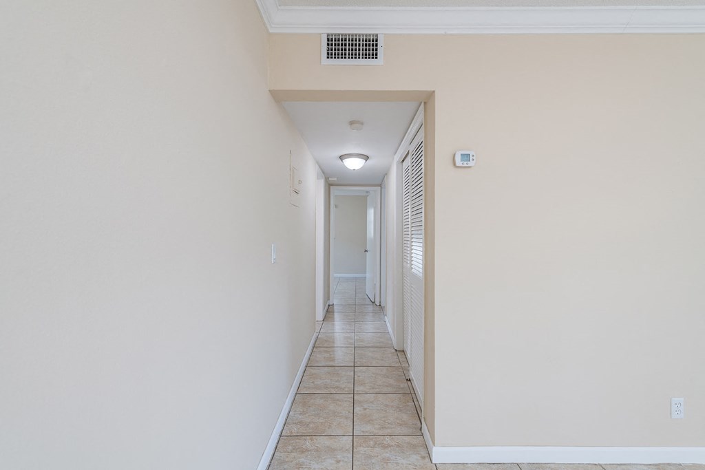 a hallway with white walls and a tile floor and a ceiling fan
