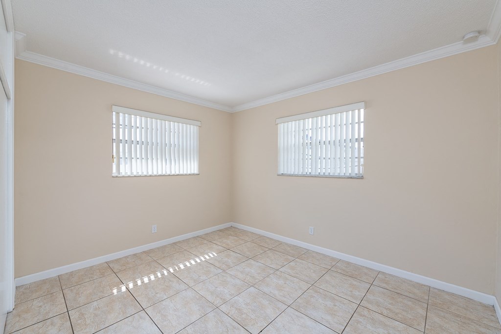 an empty living room with two windows and a tiled floor