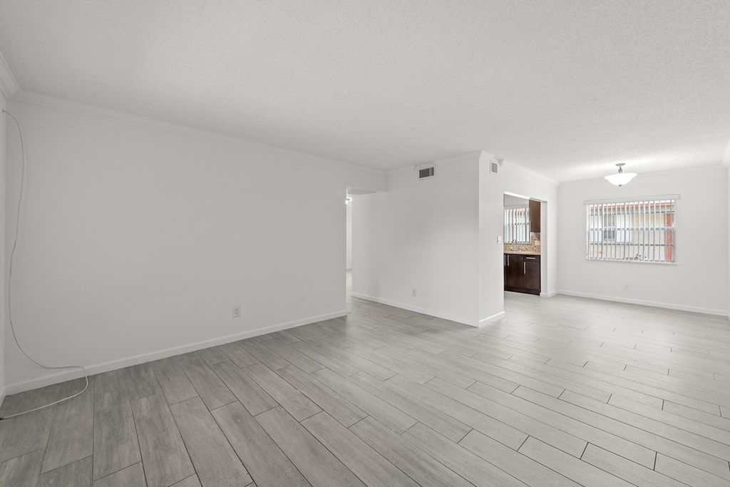 the living room and dining room of an apartment with white walls and wood floors