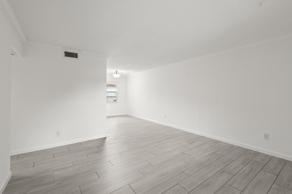 the living room and dining room of an apartment with white walls and wood flooring