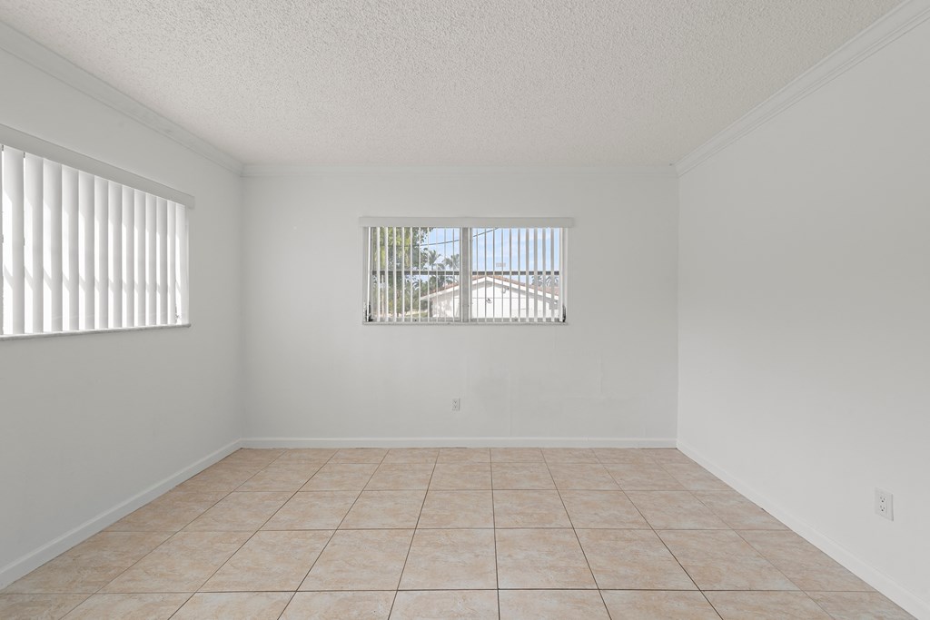 an empty living room with a tiled floor and two windows