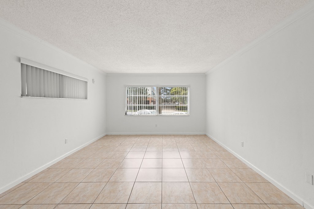 an empty living room with a window and tiled floors
