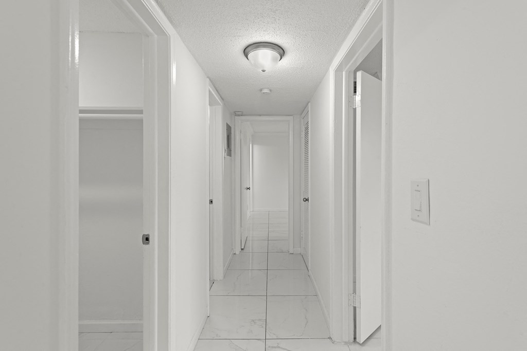 a long hallway with white walls and a white tile floor and a ceiling light