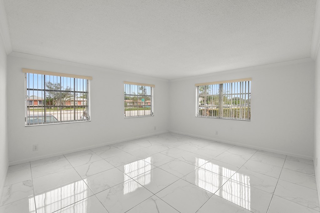 an empty living room with three windows and a tiled floor