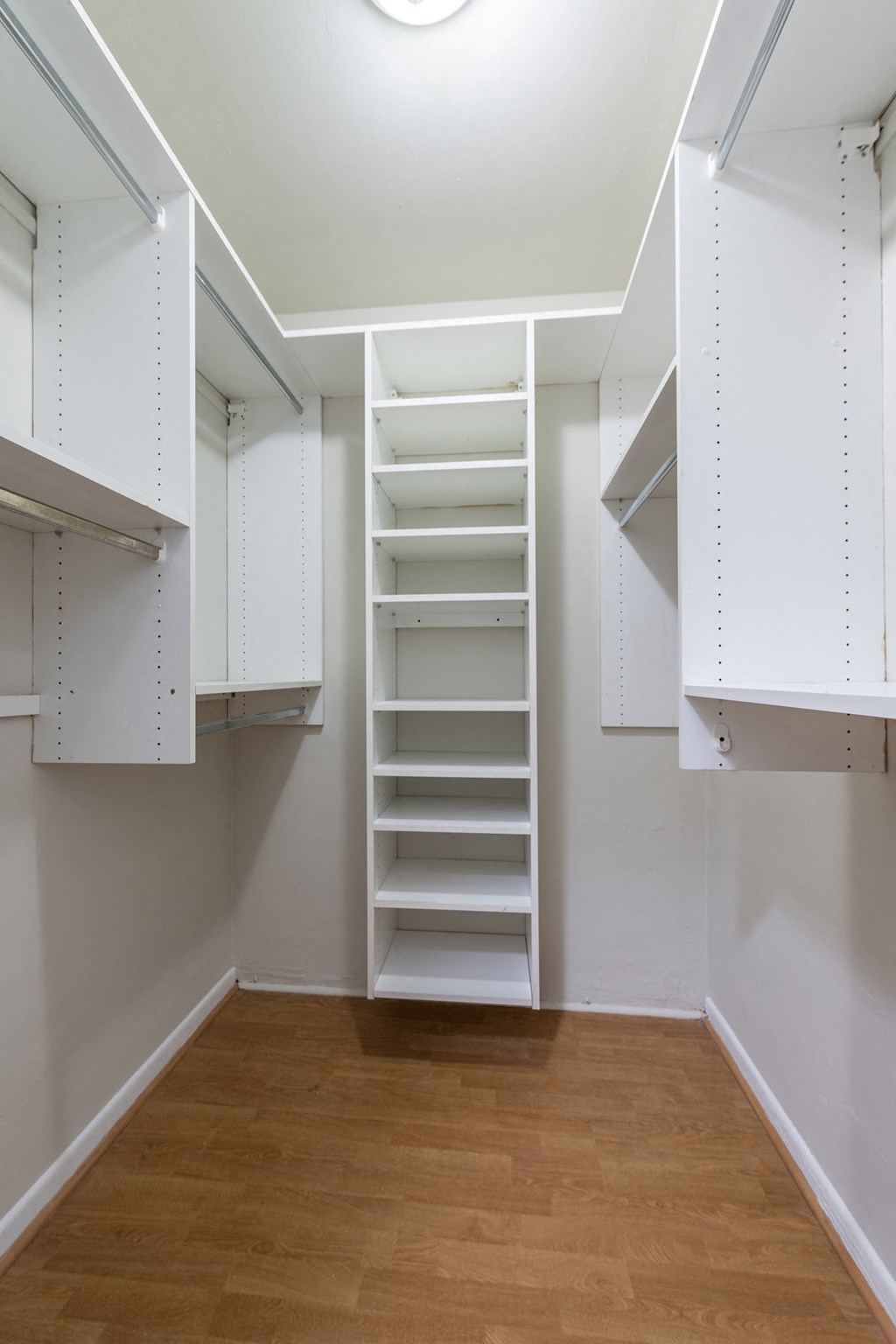 a walk in closet with white shelves and a wood floor
