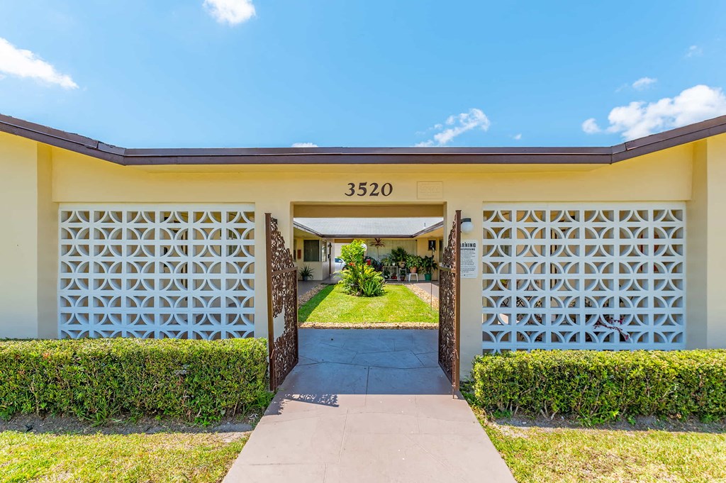 the entrance to a yellow house with a driveway and a gate
