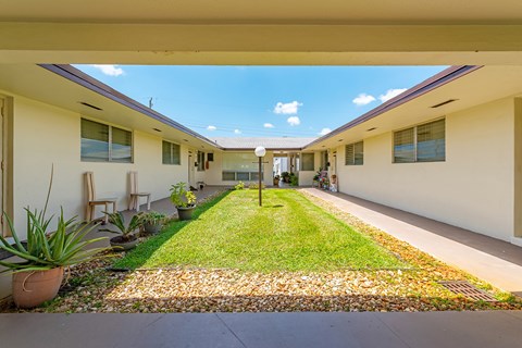 a courtyard between two buildings with a green lawn and a blue sky