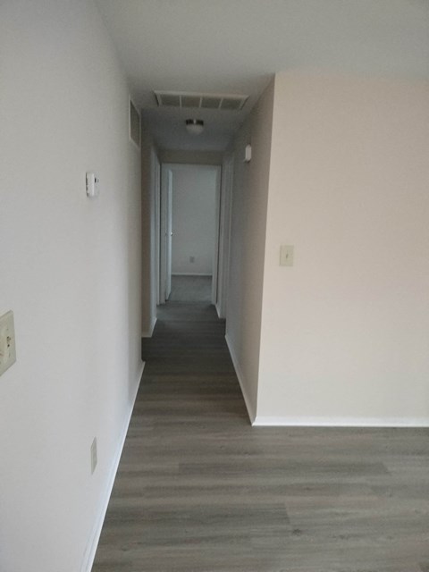 a long hallway with white walls and wood floors and a door in the distance