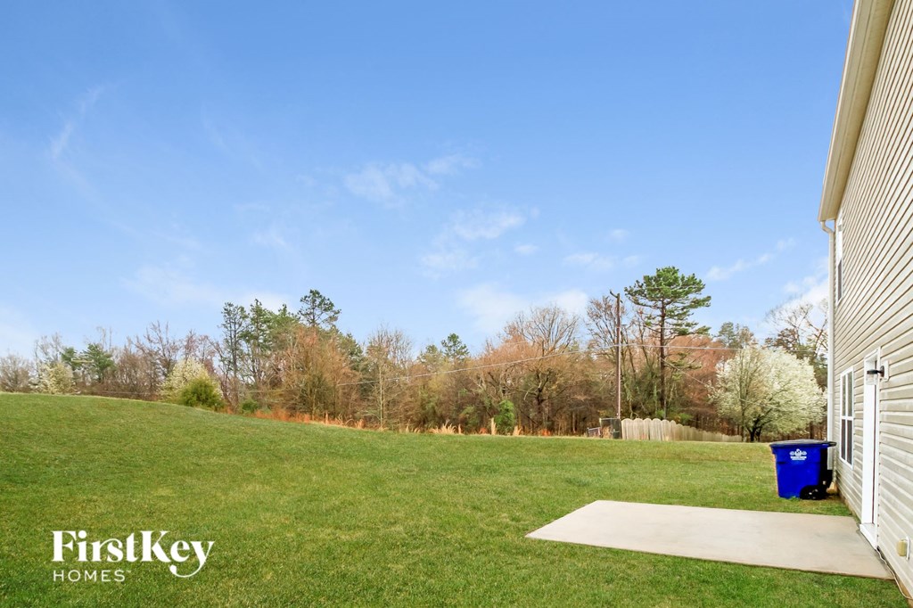 a backyard with green grass and a blue trash can