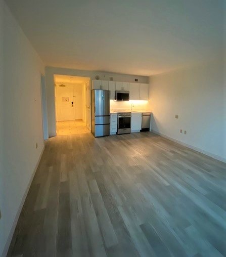 A room with a kitchen in the background and a wooden floor.