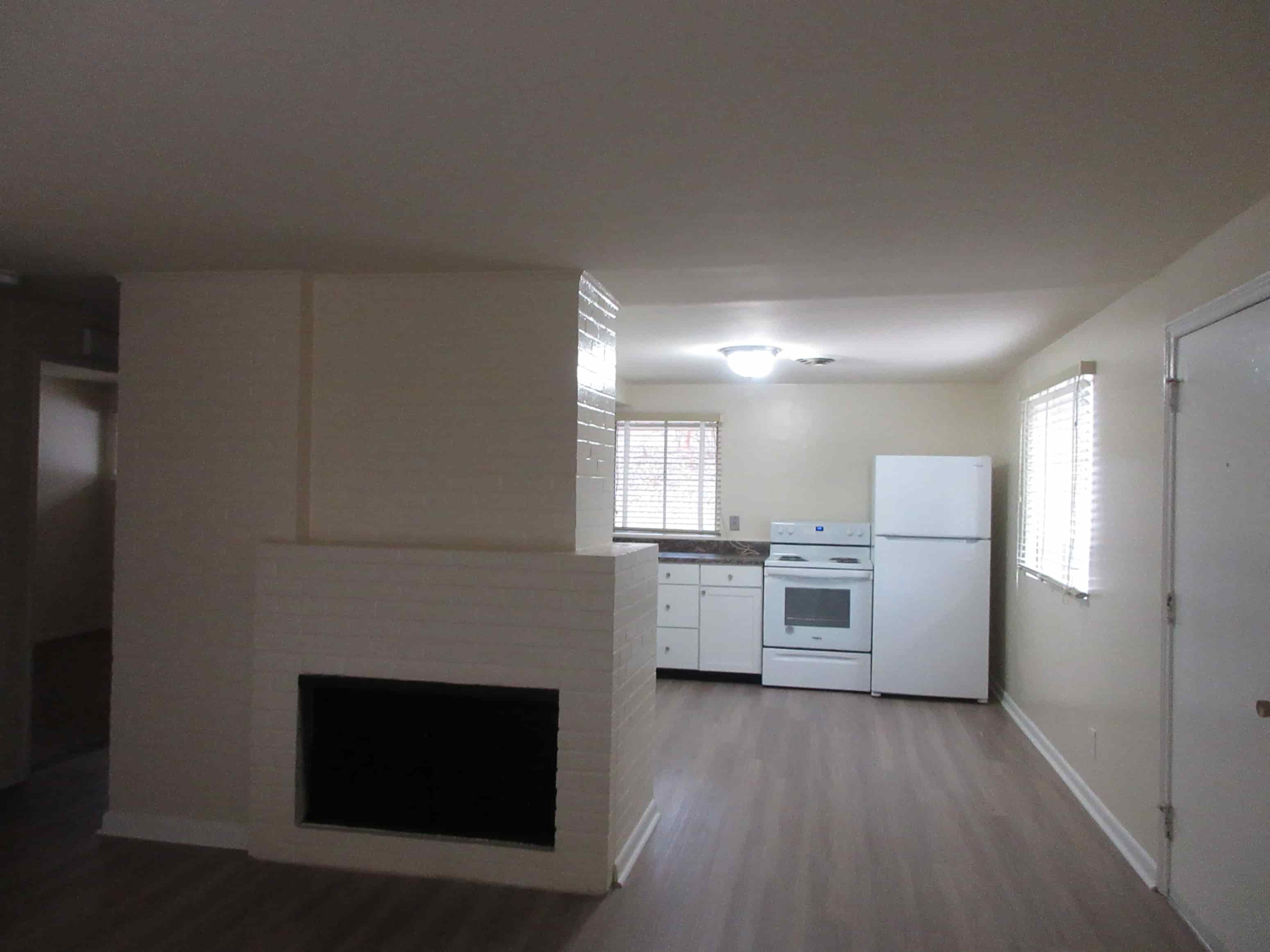 A white fireplace in a room with a refrigerator and a window.