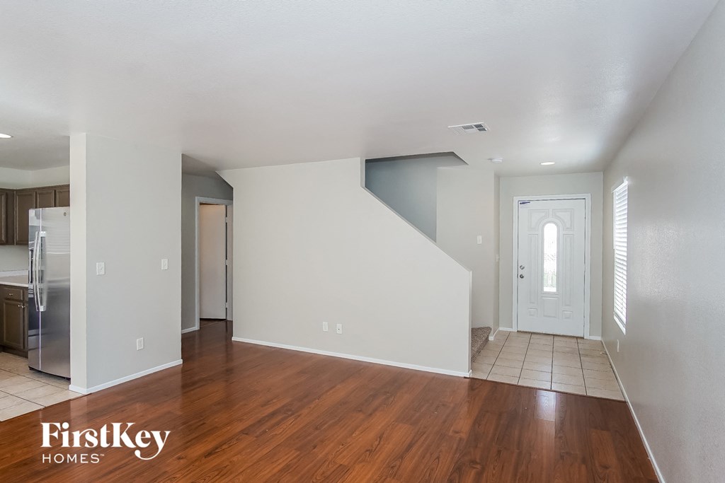 A room with wooden floors and white walls, with a staircase leading to another room.
