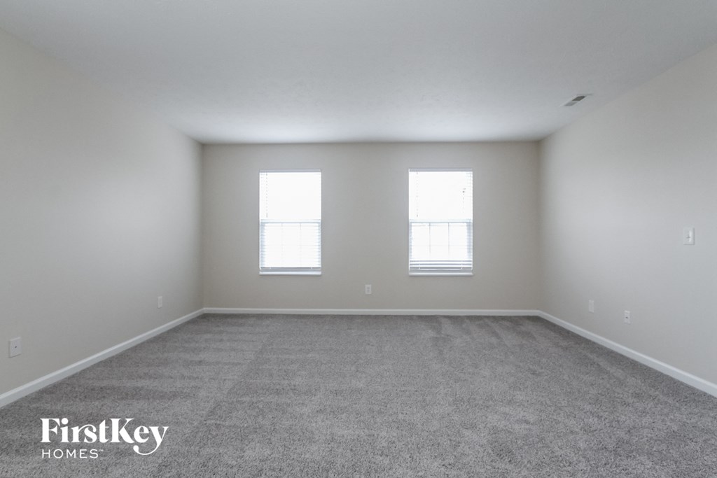 the spacious living room with two windows and carpeting