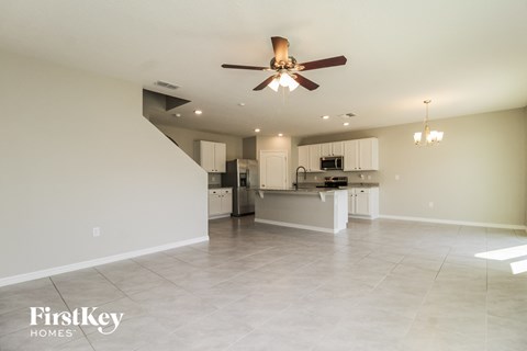 A spacious kitchen and living room with a ceiling fan and chandelier.