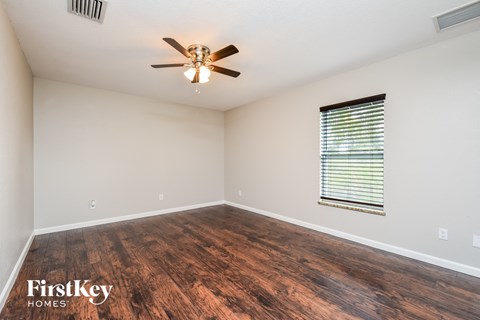 the spacious living room with hardwood flooring and a ceiling fan