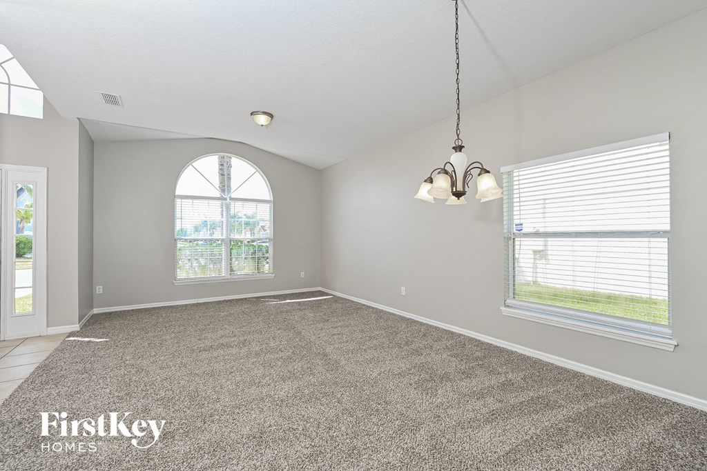 A spacious room with a grey carpet and a chandelier hanging from the ceiling.