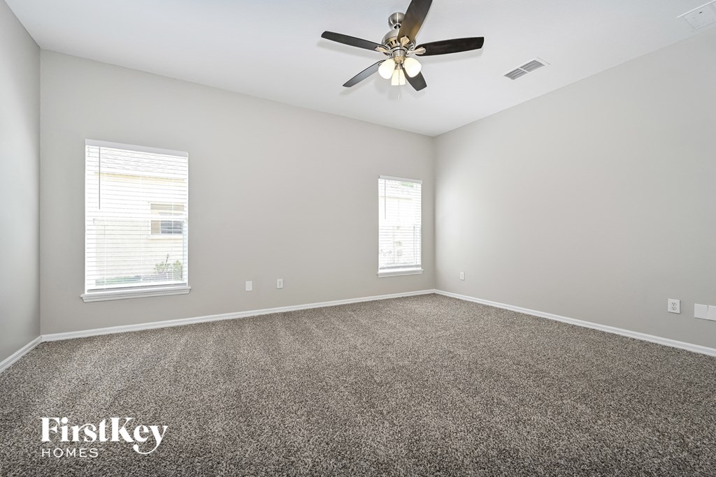 A room with a ceiling fan and two windows.
