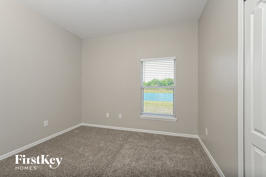 A room with a carpeted floor and a window showing a view of a pool and trees.