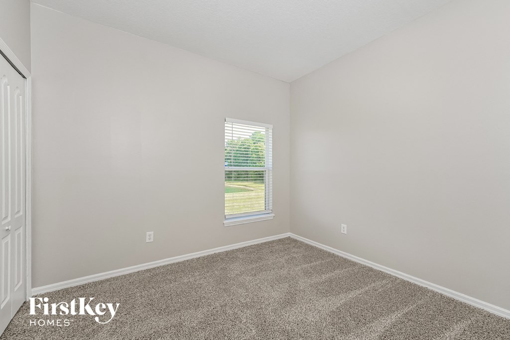 A room with a carpeted floor and a window with blinds.