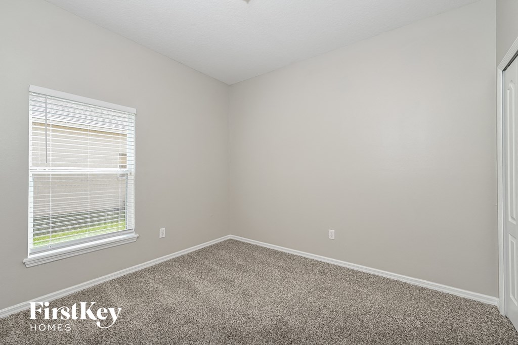 A room with a carpeted floor and a window with blinds.