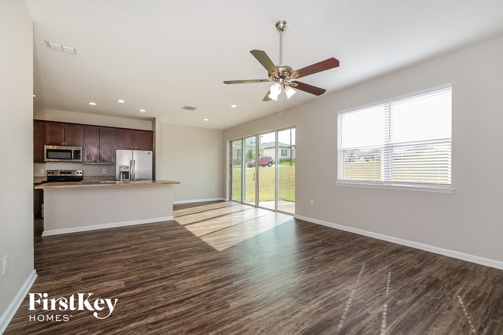 an empty living room with a ceiling fan and a kitchen