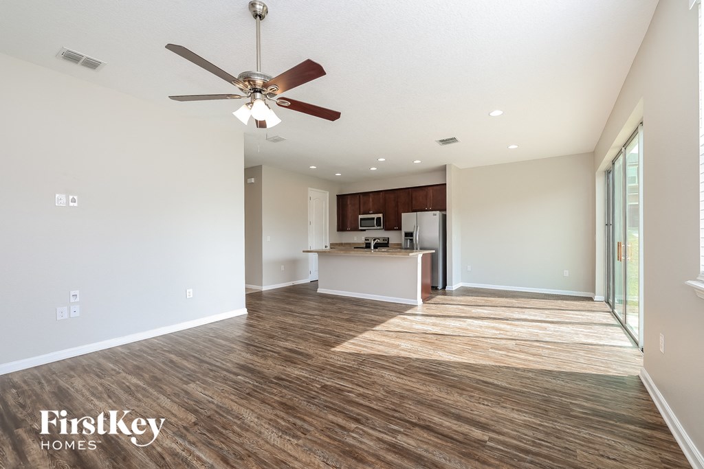 an empty living room with a ceiling fan and a kitchen