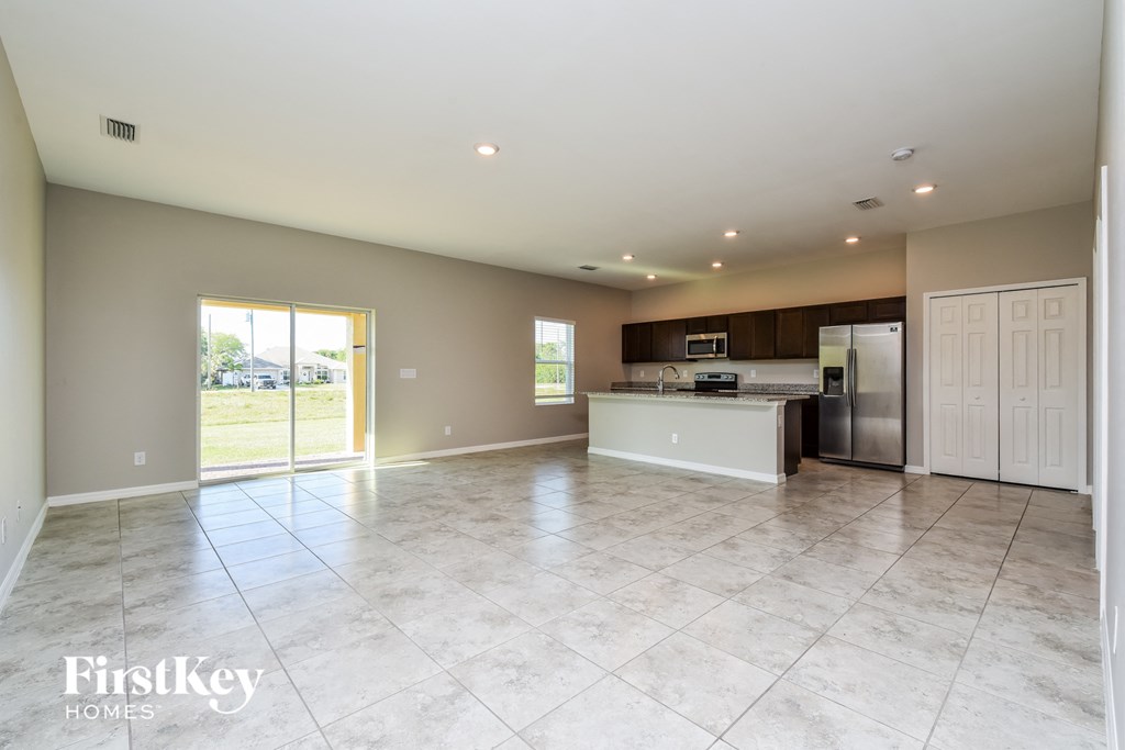 A spacious kitchen and living room with tile flooring and a sliding glass door.
