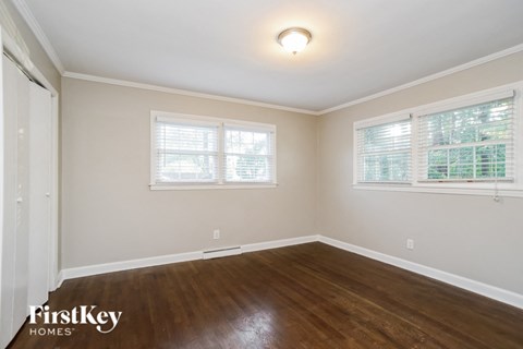 a bedroom with wood floors and white walls and two windows
