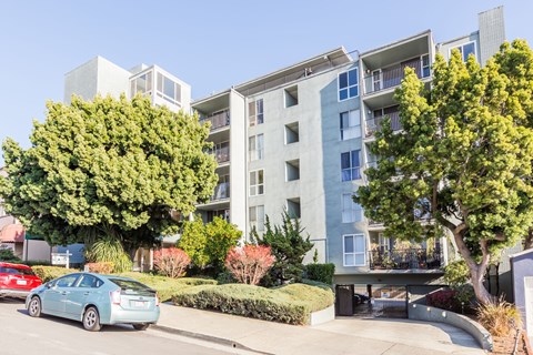 A blue car is parked in front of a modern apartment building.