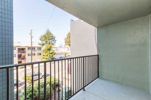 A balcony with a black railing and a view of a street with cars and buildings.