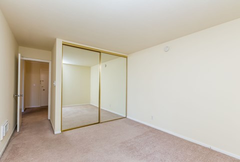 A bedroom with a carpeted floor and a mirrored door.