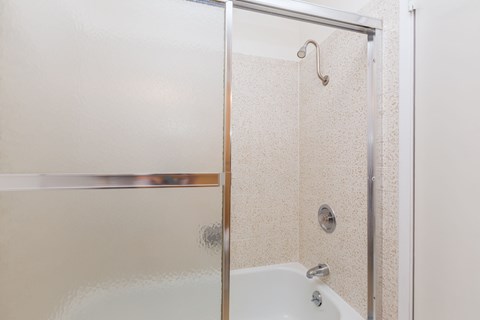 A shower with a glass door and a beige tiled wall.